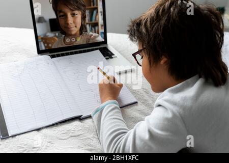 Kleiner Junge, der auf dem Bett liegt und einen Laptop für Videochat benutzt Stockfoto