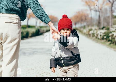 Portrait eines kleinen Jungen, der die Hand der Mutter mit rotem Bommel hält Stockfoto