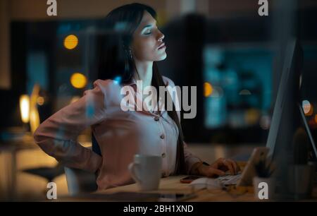 Junge Frau, die im Büro am Schreibtisch sitzt, hat Rückenschmerzen Stockfoto