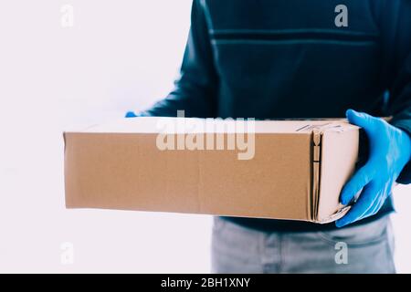 Lieferperson Lieferpaket mit blauen Latexhandschuhen als Sicherheitsmaßnahme für das Coronavirus. Lieferer in Quarantänezeit mit Kopierraum. Stockfoto