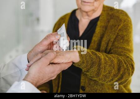 Arzt, der Salbe auf die Hand des älteren Patienten legt Stockfoto