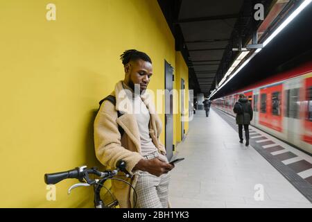 Stilvoller Mann mit Fahrrad und Smartphone in einer U-Bahnstation Stockfoto