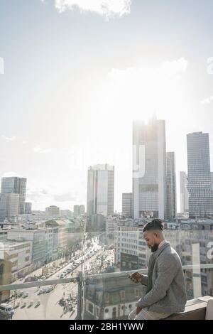 Stilvoller Mann mit Smartphone auf Aussichtsterrasse mit skycraper-Blick, Frankfurt, Deutschland Stockfoto