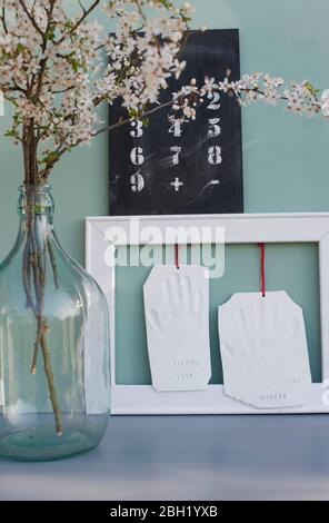 Tonhanddrucke hängen im Bilderrahmen, Tafel mit Zahlen und blühenden Schlehdornzweigen Stockfoto