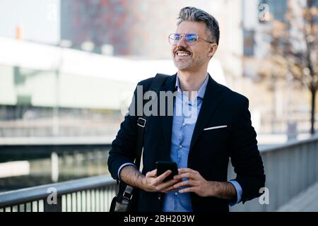 Lächelnder grauhaariger Geschäftsmann mit Handy in der Stadt Stockfoto