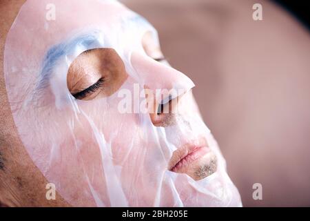 Nahaufnahme eines schönen kaukasischen Mann trägt eine Bio-Zellstoff-Blatt-Maske, während entspannt Stockfoto