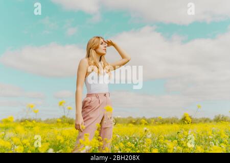 Junge Frau, die im Frühling auf einer Blumenwiese steht und nach draußen schaut Stockfoto