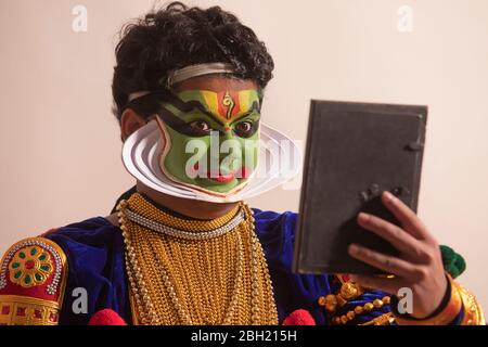 Kathakali Tänzer sitzt vor weißem Hintergrund und überprüft sein Make-up im Spiegel. Stockfoto