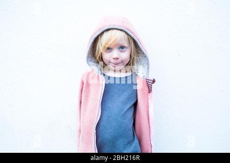 Portrait von kleinen blonden Mädchen trägt rosa Kapuzenjacke vor der weißen Wand Stockfoto