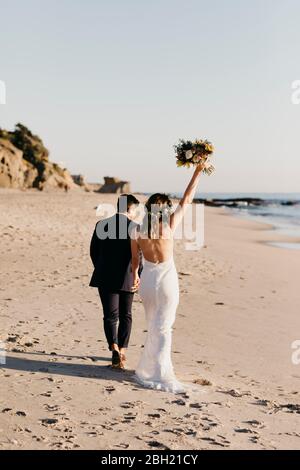 Rückansicht des glücklichen Brautpaares, das am Strand läuft Stockfoto