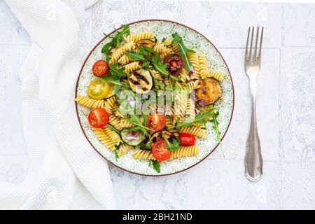 Teller mit vegetarischen Nudelsalat mit gegrillten Zucchini, Tomaten, Rucola, roten Zwiebeln und Balsamico-Essig Stockfoto