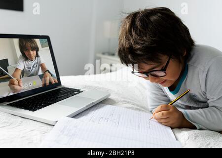 Kleiner Junge, der auf dem Bett liegt und einen Laptop für Videochat benutzt Stockfoto