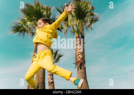 Kleines Mädchen, das vor Palmen in die Luft springt Stockfoto