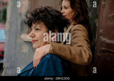 Lächelnde ältere Frau und ihre Erwachsene Tochter im Hintergrund, die aus der Ferne schaut Stockfoto