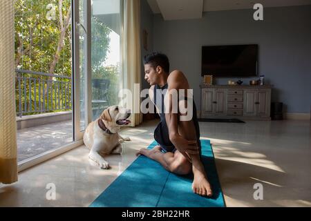 Mann macht Yoga-Übungen, während sein Hund ihn beobachtet. Stockfoto