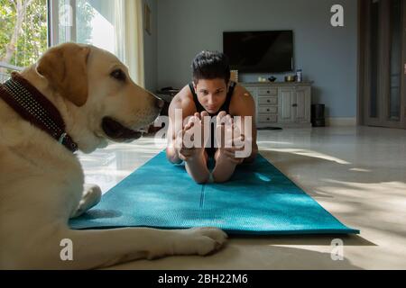 Mann, der Yoga-Übungen macht und sein Hund mit ihm sitzt. Stockfoto