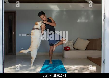 Mann, der während der Übungen auf seiner Yogamatte steht und seinem Hund Leckereien gibt. Stockfoto