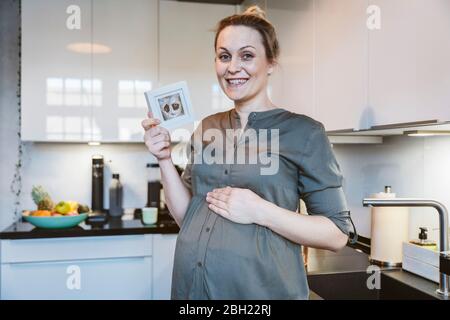 Portrait der schwangeren Frau in der Küche zu Hause halten Ultraschall-Bild Stockfoto