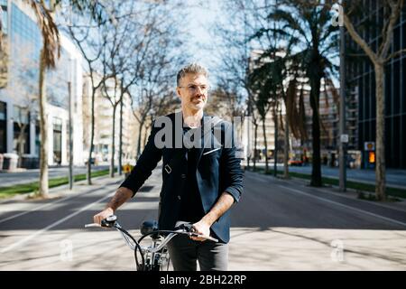 Grauhaariger Geschäftsmann, der sein Fahrrad in der Stadt schiebt Stockfoto