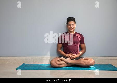 Mann sitzt auf der Yogamatte und macht Übungen. Stockfoto