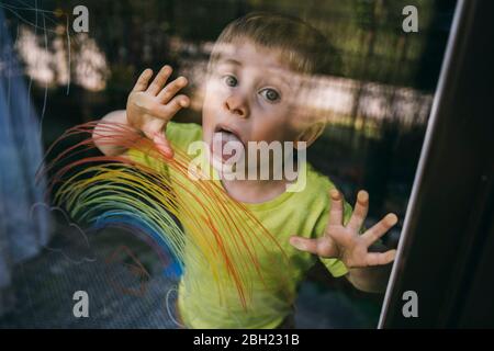 Portrait des kleinen Jungen hinter Balkontür lecken Glasscheibe mit gezeichneten Regenbogen Stockfoto