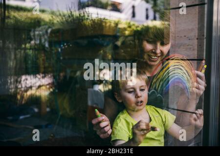 Mutter und kleiner Sohn zu Hause zeichnen Regenbogen auf dem Fenster Stockfoto