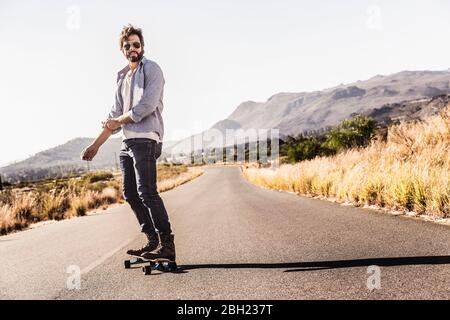 Mann, der Skateboard auf Landstraße reitet Stockfoto