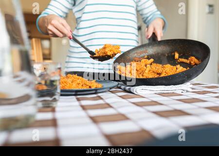 Frau serviert Pasta auf dem Teller zu Hause Stockfoto