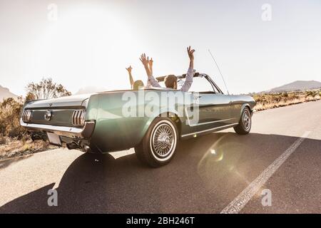 Glückliches Paar mit erhobenen Armen im Cabrio-Auto auf einer Reise Stockfoto