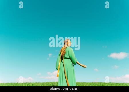 Junge Frau mit verbundenen Augen in einem grünen Kleid auf einem Feld stehend Stockfoto