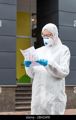 Porträt der müde erschöpft Ärztin, Wissenschaftlerin oder Krankenschwester trägt Gesichtsmaske und biologische Hasmat psa Anzug Lesung WHO Behandlungsprotokoll oder Stockfoto