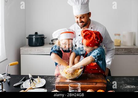 Vater mit zwei Kindern, die Teig in der Küche zu Hause vorbereiten Stockfoto