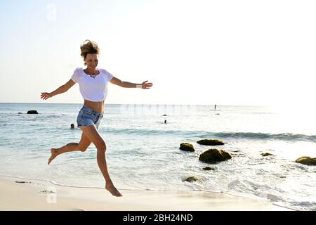 Schöne Frau läuft und springt vor Freude am Strand Stockfoto