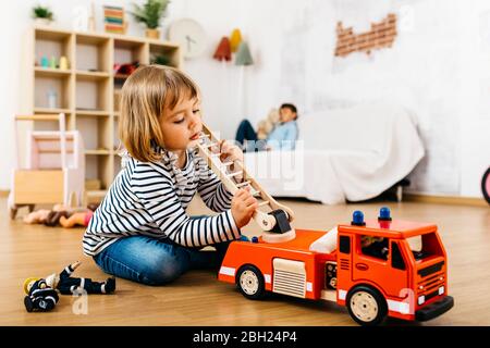 Kleine Blondine spielt mit einem hölzernen Feuerwehrauto Stockfoto