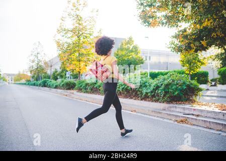 Junge Frau mit Afro-Frisur läuft auf einer Straße in der Stadt Stockfoto