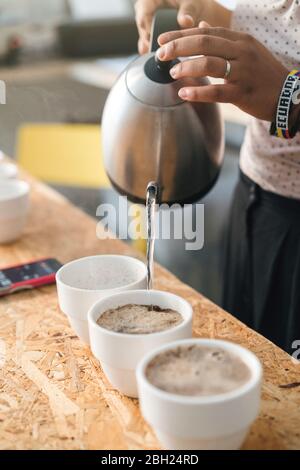Nahaufnahme einer Frau, die in einer Kaffeerösterei arbeitet und heißes Wasser in Kaffeetassen gießt Stockfoto