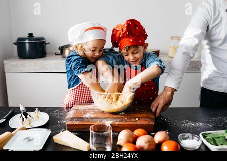 Kinder bereiten Teig mit Vater in der Küche zu Hause Stockfoto