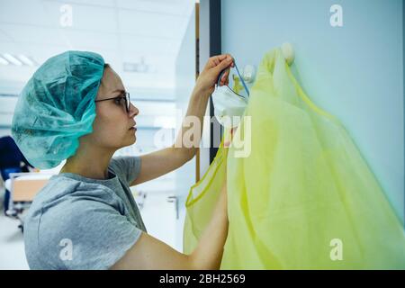 Arzt, der persönliche Schutzausrüstung aus dem Haken im Krankenhaus nimmt Stockfoto