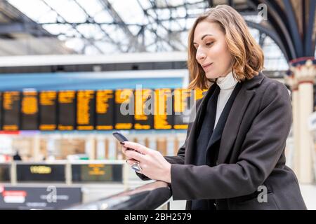 Frau am Bahnhof mit Mobiltelefon, London, Großbritannien Stockfoto