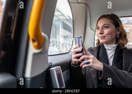 Geschäftsfrau im hinteren Teil eines Taxis, die aus dem Fenster schaut, London, Großbritannien Stockfoto