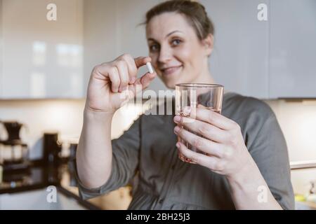 Portrait einer Frau, die Pille und Glas Wasser in der Küche zu Hause hält Stockfoto