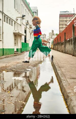 Junge Frau, die auf einer Straße über Pfütze springt Stockfoto