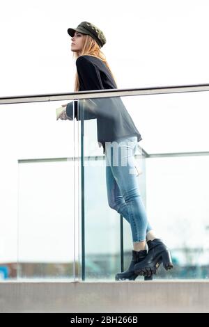Portrait der blonden jungen Frau, die auf dem Geländer lehnt und in der Ferne schaut Stockfoto