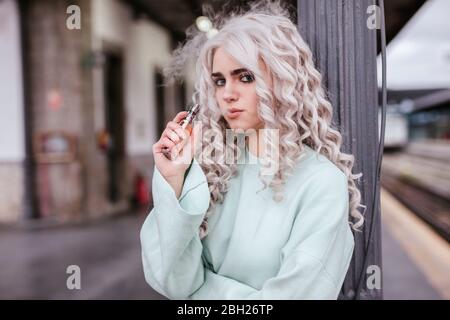 Portrait einer jungen Frau, die elektronische Zigarette auf der Plattform raucht Stockfoto