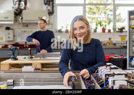 Portrait einer lächelnden Elektrikerin, die in der Werkstatt an Schaltkreisen arbeitet Stockfoto