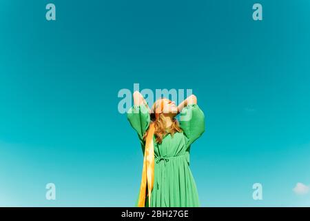 Junge Frau mit verbundenen Augen in einem grünen Kleid unter blauem Himmel Stockfoto