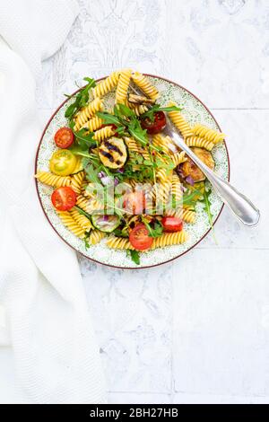 Teller mit vegetarischen Nudelsalat mit gegrillten Zucchini, Tomaten, Rucola, roten Zwiebeln und Balsamico-Essig Stockfoto