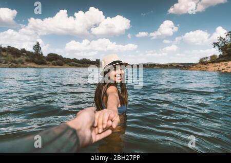 Porträt einer glücklichen jungen Frau, die in einem See baden und dabei die Hand ihres Freundes hält Stockfoto