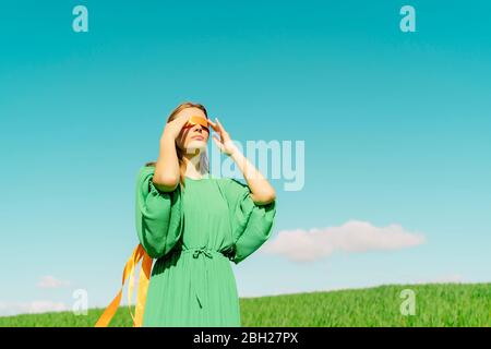 Junge Frau mit verbundenen Augen in einem grünen Kleid auf einem Feld stehend Stockfoto