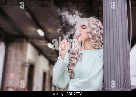 Junge Frau, die elektronische Zigarette auf der Plattform raucht Stockfoto